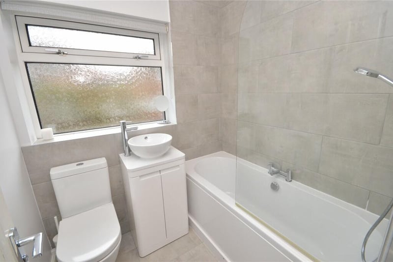 The tiled house bathroom has a bathtub with shower over, wash hand basin and WC.