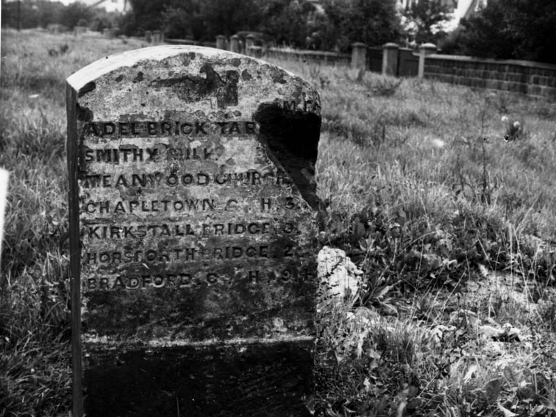 A milestone in a field at the junction of Otley Road and New Adel Lane. Part of the stone is missing on the right but reads in miles and furlongs 'Adel Brick Tar, Smithy Mill, Meanwood church, Chapeltown church 3, Kirkstall bridge 3, Horsforth bridge 2, Bradford church 9.4'. Semi detached houses and trees to right. Pictured in