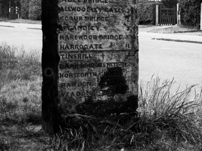 A view taken at top of Farrar Lane of a wide, arched milestone. Distance is given in miles and furlongs - reading 'Adel Bridge 6f, Alwoodley Gates 3m, Eccup Bridge 2m, Weardley 3m 4f, Harewood Bridge 5m 2f, Harrogate 11m 2f, Tinshill church 1m, Parr Bridge station 2m, Horsforth church 3m, Rawdon church 3m 4f, Yeadon church 5m'. Pictured in July 1950.