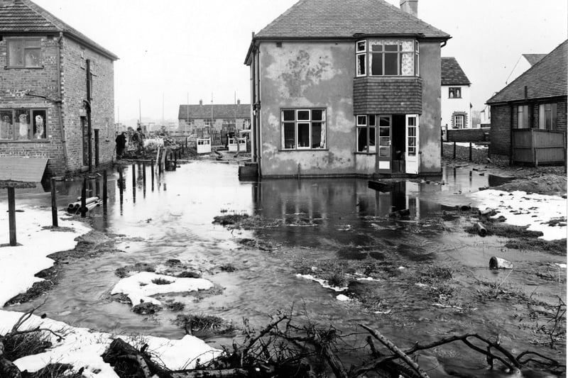 The back of number 53 Kingsley Avenue; a detached house which has been flooded with water from the nearby fields. Adjacent houses are visible, as are workmen on the left. Pictured in February 1953.