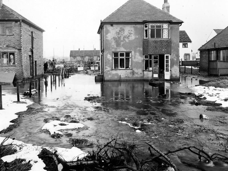 The back of number 53 Kingsley Avenue; a detached house which has been flooded with water from the nearby fields. Adjacent houses are visible, as are workmen on the left. Pictured in February 1953.