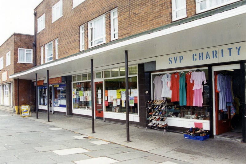Heights Drive showing nos.34 to 40. On the right is the SVP Charity Shop at no. 34, with clothes and shoes displayed outside. Next to this, no. 36 is Armley Heights Library, one of Leeds City Libraries' small branches, then at no. 38 is Dewhirsts Newsagents and Post Office.