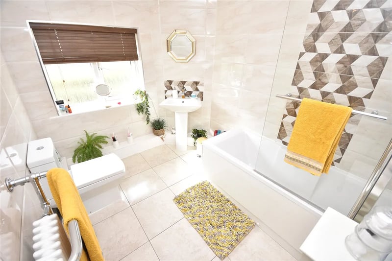 The fully tiled house bathroom has a contemporary three-piece suite in white with shower head and screen over the bath.