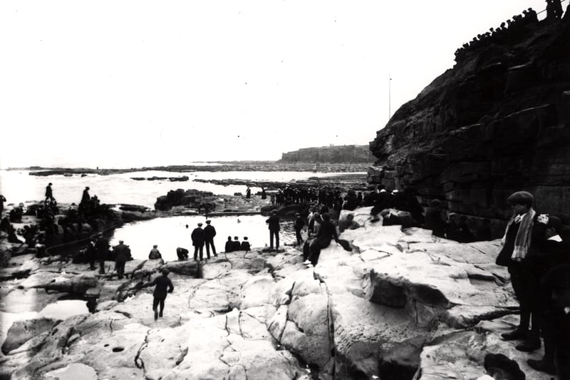 People standing on the rocks watching swimmers in the pool in 1925.
