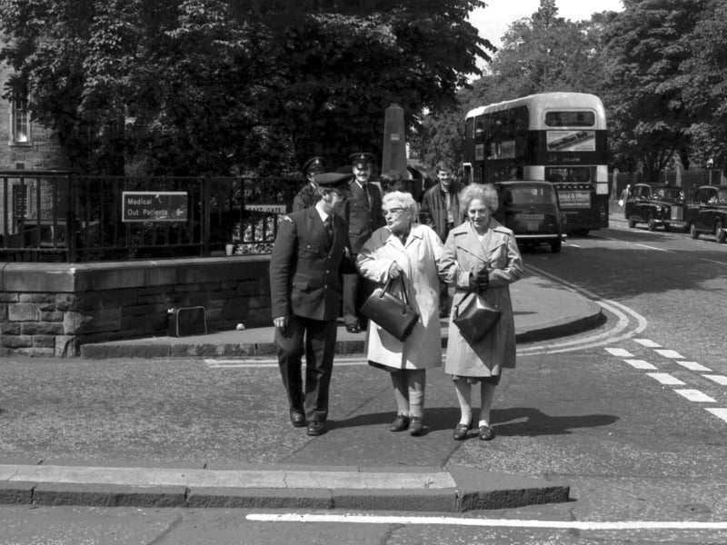 An ambulance driver leaves the Edinburgh Royal Infirmary picket line to help two old ladies across the road during the ambulancemen's strike of July 1981.