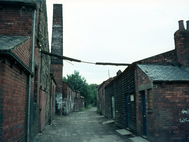 Derelict buildings of Woodlands Dyeworks on Wood Lane, including a tall chimney, taken shortly before their demolition. Also known as Crowther's Mill, the dyeworks had been the business of the Crowther family since Edward Crowther took over the site in 1906, though the mill itself is believed to have dated back to about 1601. Pictured in July 1975.