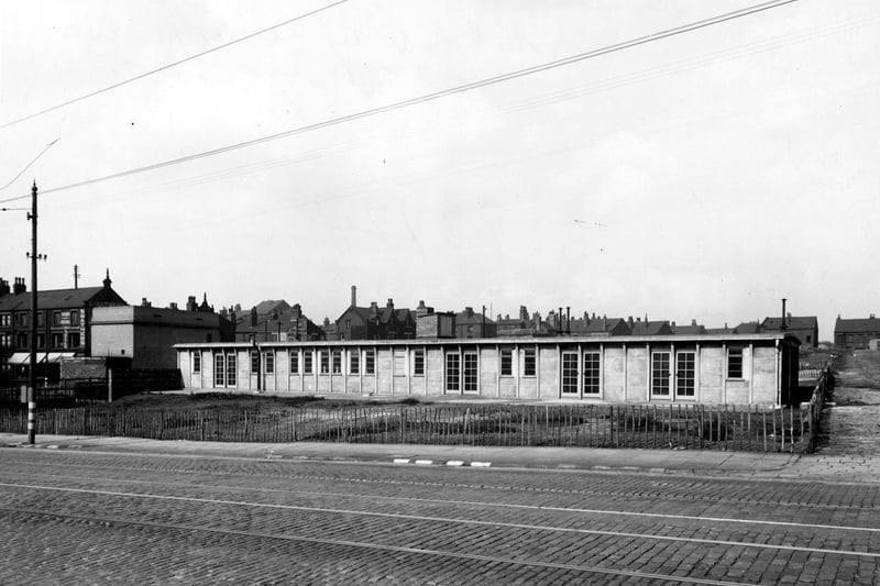 the day nursery on York Road. The building is a one story building with many doors and windows. A rickety wooden fence is visible around the nursery. 'Smathers, beds and suit shop', is visible on the right. Tramtracks and cables can be seen. Pictured in September 1943.