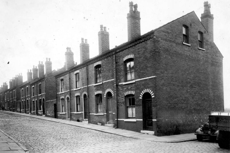  Looking south-west along the west side of Bickerdike Street, a brick terraced row with black and white painting above the doors and windows. There is a car and a lorry on the far right where the junction with Bickerdike Road is visible. Pictured in July 1949.