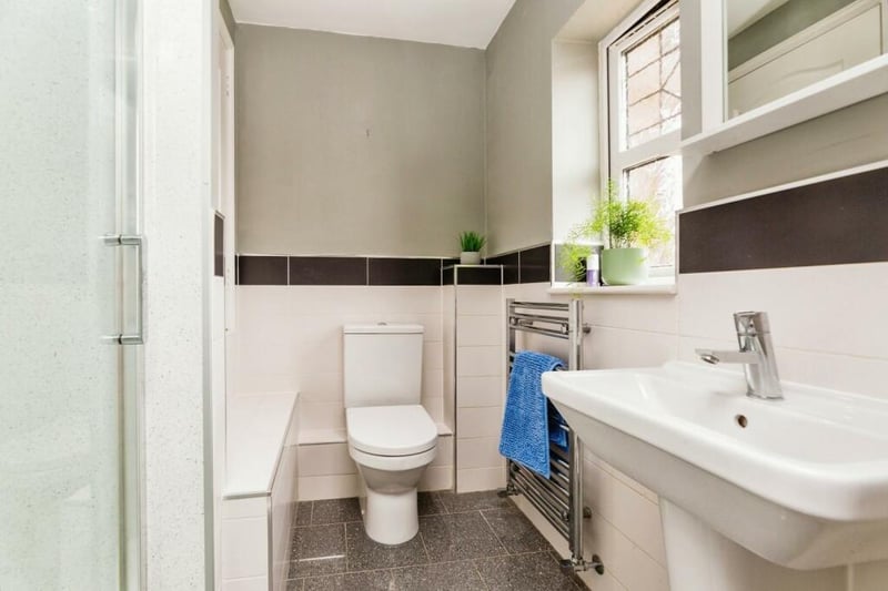 Tiled in sleek, monochrome tones, hosting a glass shower cubicle, white pedestal sink, low flush WC, wall mounted chrome heated towel rail, tiled flooring, large built in storage cupboard, inset spotlights, extractor fan and frosted uPVC window.