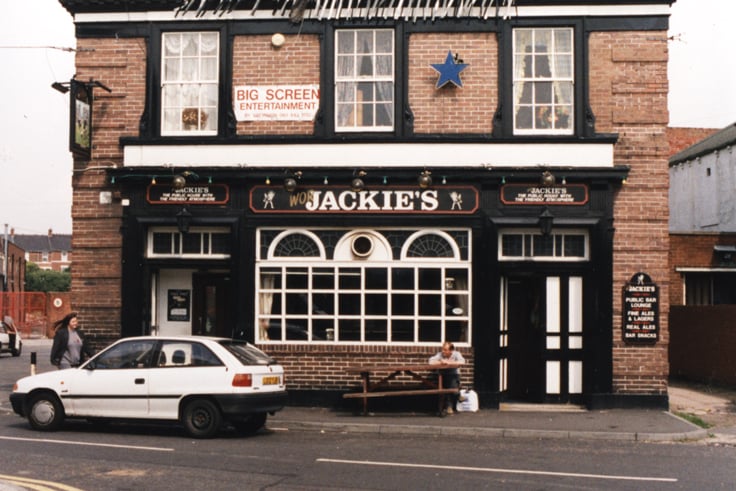  A photograph of the frontage of Jackie's pub in Byker in 1996. A banner has been strung across the top of the building with the slogan 'Win or Lose we'll have some BOOZE! Two replicas of the FA cup are sitting on plinths on either side of the roof. 