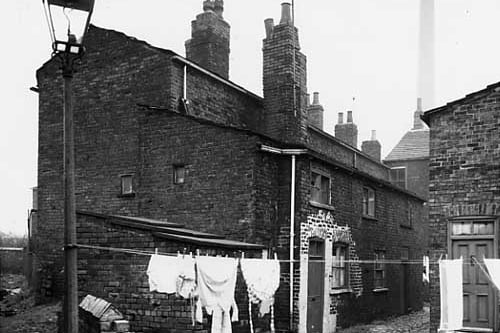 Knowles Street in November 1963. On the left can be seen the end of the row which was Knowles Yard. A lamp post supports washing lines, a block of outside toilets is between the houses and the washing line. Number 78 Knowles Street has the highly visible pointing around the door and window.