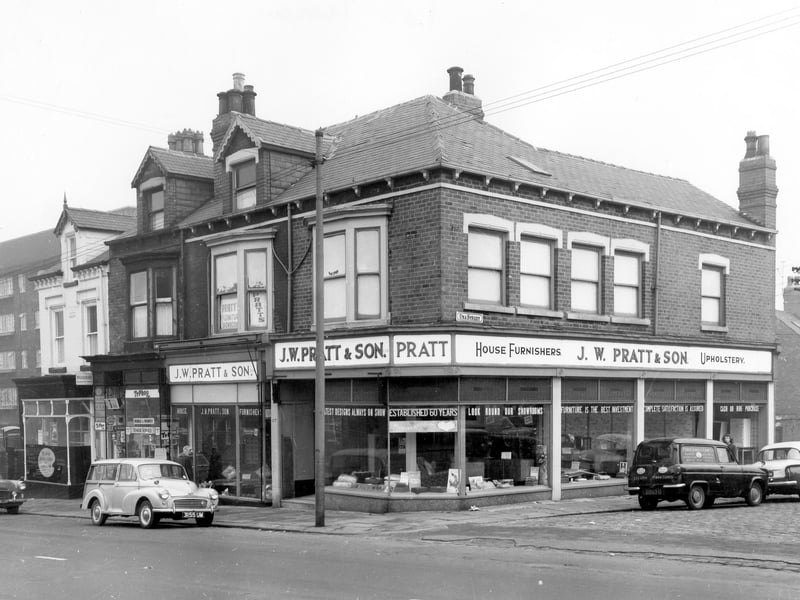 Beeston Road in October 1963. The shops on Beeston Hill including at number 101 (just visible) Marsh Jones & Cribb Ltd, painting contractors. At number 103 is a grocers advertising cigarettes and Typhoo Tea. On the right at numbers 105 & 107 is V.W. Pratt & Son, house furnishers and upholstery. Advertised in the window are 'The latest designs always on show'. On the right cars including the Una Street while more cars are parked on Beeston Road.