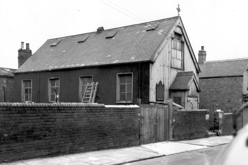 the Good Physician Church of England Mission Room on Folly Lane. Two ladders are propped up against the side wall of the hall on the left while on the right is the gable end with entrance porch and notice board. An iron cross stands on the ridgepole of the hall and on the far right can be seen number 10 Folly Lane. Pictured in October 1963.