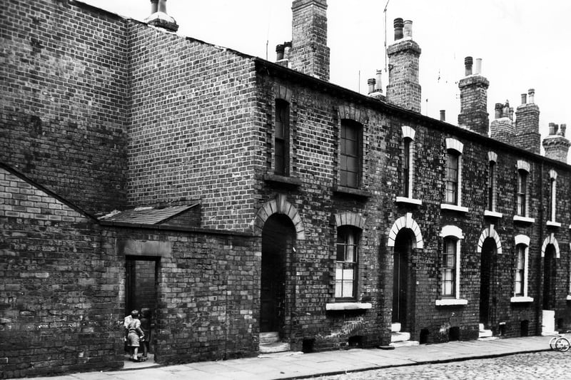 Arkwright Street in October 1963. A row of back-to-back terraced houses with a yard on the left housing a shared outside toilet block. Children can be seen through the doorway to the yard. 