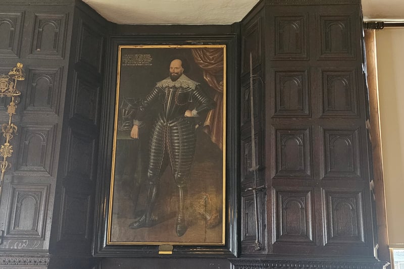 Located next to the portrait of Sir Hugh Smyth Knight in the Great Oak Room, the golden stand on the wall would have been used as a sword holder.