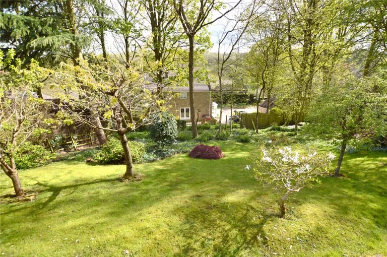 The beautifully landscaped garden has a tree-lined lawn with shrubs.
