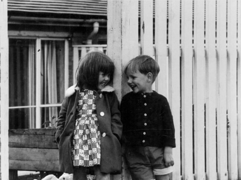 Two children laughing together outside a house believed to be on Raeburn Road, Herdings, Sheffield, during the 1960s