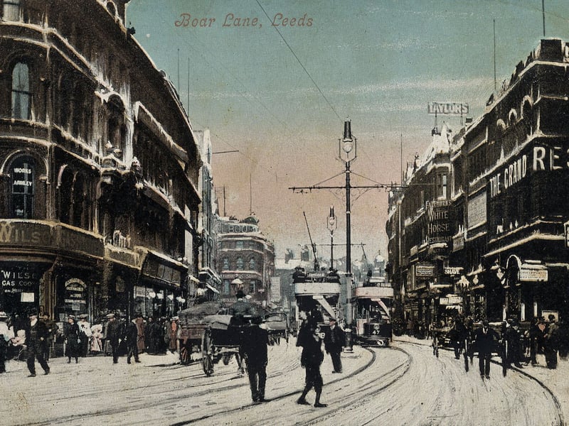 A postcard view looking east along Boar Lane. On the left, by the junction with Albion Street, is Wilsons Ltd., gas cookers and stoves. On the right, after the junction with Alfred Street, is the Grand Restaurant, with Fairburn's White Horse Restaurant further along. Many people are out and about despite a covering of snow on the ground.