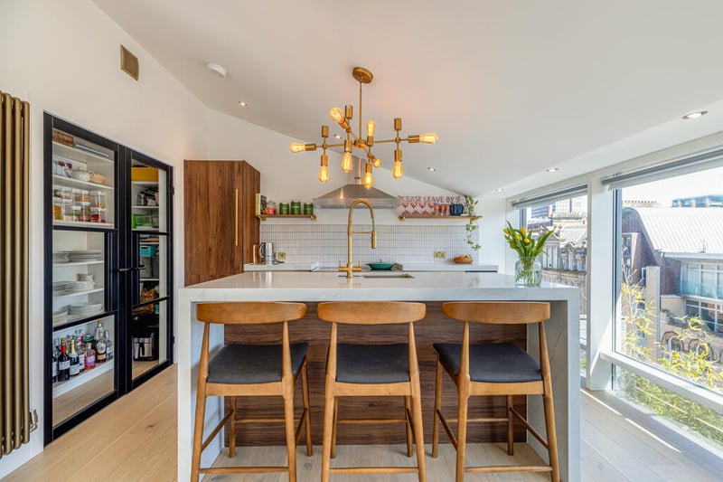 The modern kitchen features 3 oven range cooker, a marble waterfall island inset with sink with gold crosswater tap and a shelved pantry set behind stylish Crittall style doors. 