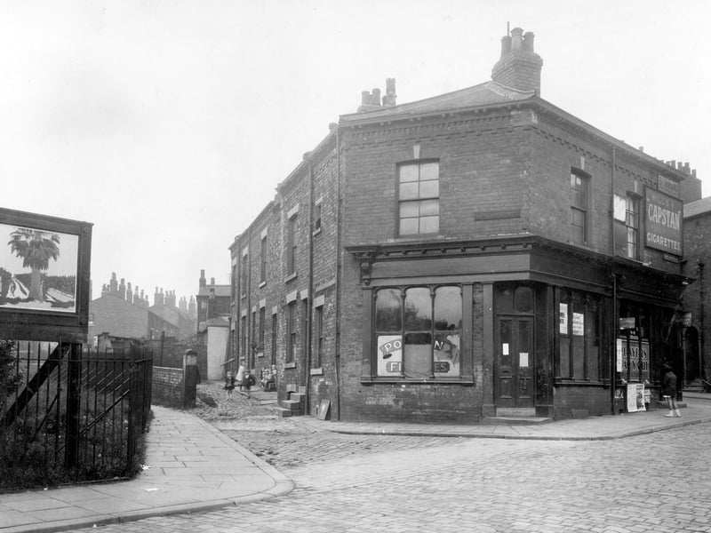 Sunny Bank Street pictured in July 1930. This area was to be site for the new Leeds Civic Hall. To the left, corner of open public green, on the right, a tobacconists shop, premises of a fish and chip shop in the centre.