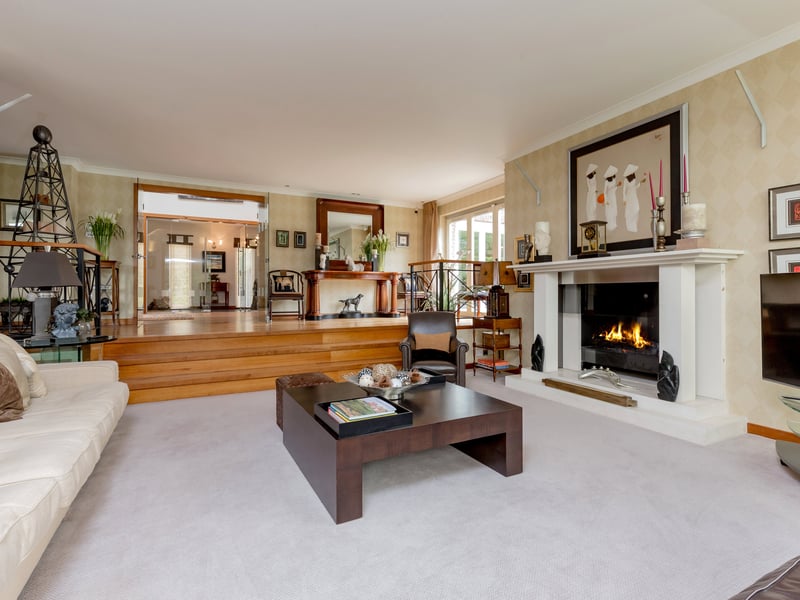 Interior: The property benefits from a vast amount of space and includes a sitting room with full-height glazing on one side, a kitchen with large island, five bedrooms over two floors, and a family room adjacent to the pool area.