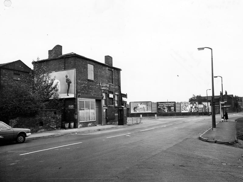 Cross Green Lane looking south east, showing junction with Ark Street in the foreground. A. Lightfoot, clothiers is at No. 43 in the centre, by the junction with Easy Road. There are advertising hoardings by the road and a telephone kiosk and bus shelter in view. Pictured in October 1978.