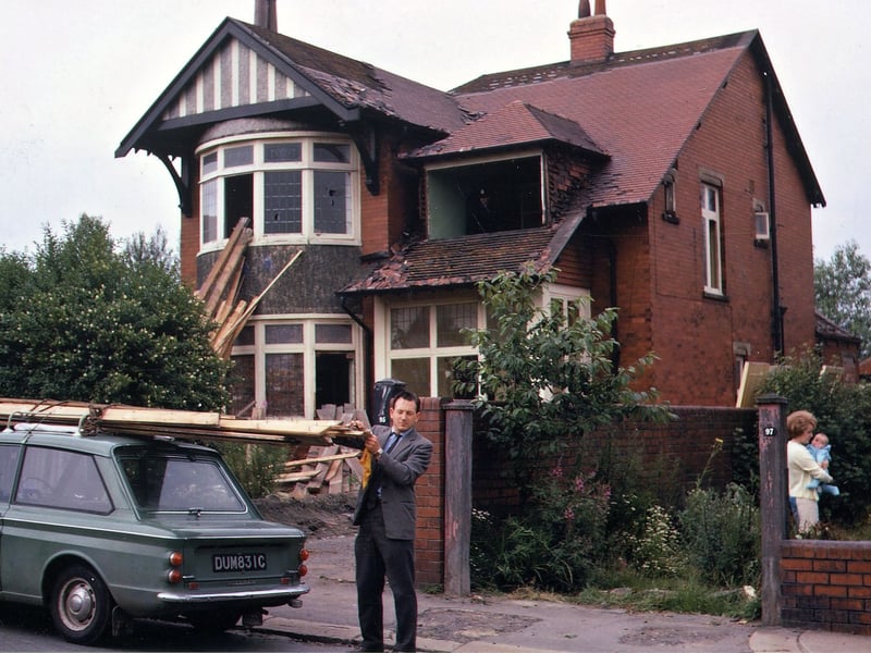 Number 95 Rein Road, a detached red brick property, in the process of being demolished to make way for the new bridge crossing the motorway. A woman holding a young baby is seen in the garden of number 97, which is also scheduled for demolition. In the foreground a man is loading the roof of his car with timber from the derelict house. Pictured in July 1968.