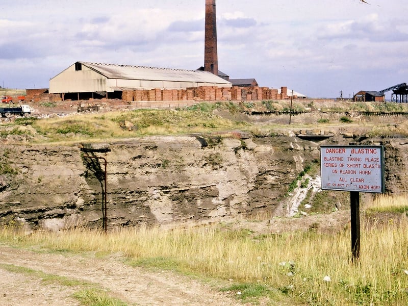 A brickworks and disused quarry at Woodkirk. A warning notice says 'Danger Blasting. Blasting taking place. Series of short blasts on klaxon horn. All clear.' Bricks are stacked along the side of the building and there is a tall brick chimney. Pictured in August 1967.