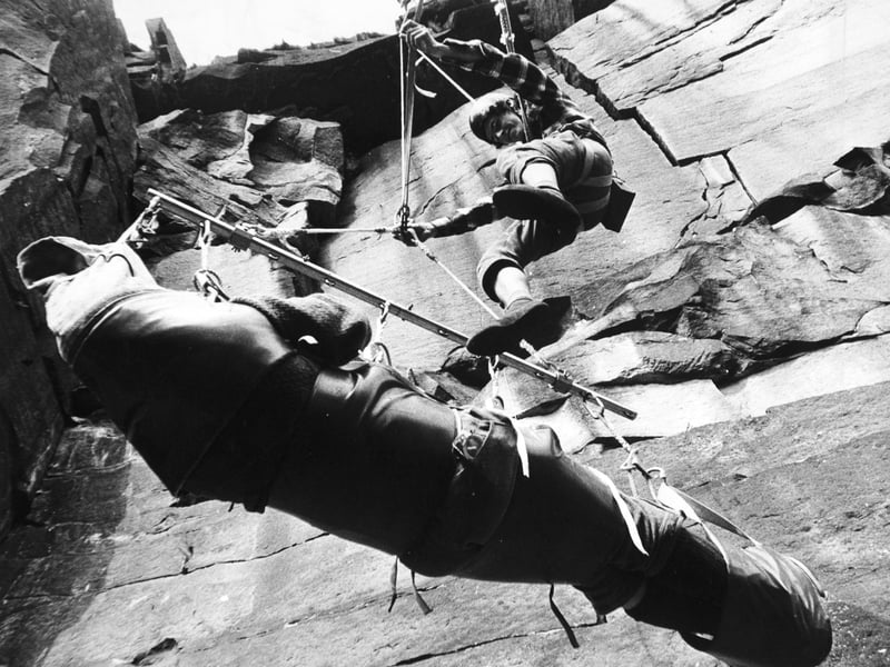 Testing a new type of stretcher at Heptonstall Quarry in August 1974 for lowering injured climbers from high crags. Firmly trussed up in the stretcher is Douglas Brill, Calder Valley Moorland Rescue team leader. Above him dangles Clive Green, who is guiding the stretcher down the 120ft. face of the quarry.