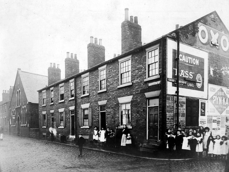 The junction of Bristol Street and Cross Stamford Street. Painted signs and Playbills are visible on side of house the most prominent being for Oxo and Bass Carling label. Children are gathered on the corner in period dress. 4 properties 3 with downstairs window shutters with United Methodist Free Church (Providence Chapel). Pictured in July 1903.