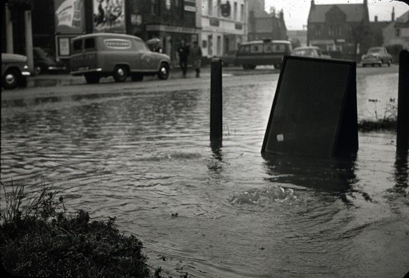Bondgate during severe flooding which took place in the summer of 1961. The near side of the road is deep in water. Across the road are Garbutt and Mawson Ltd., ironmongers, then the Bowling Green pub. The junction with Crossgate is on the right.