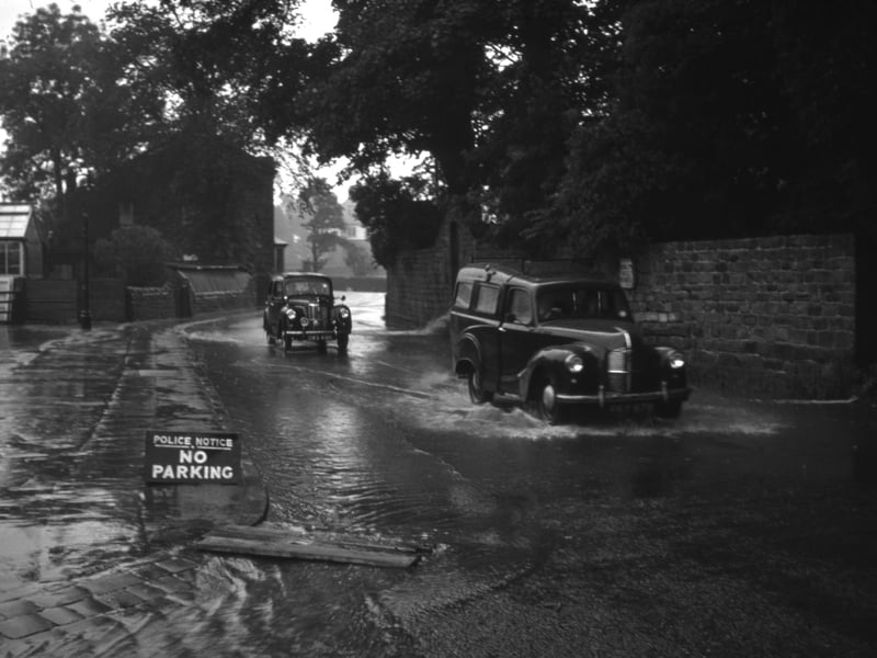 Two cars being driven through floods on Farnley Lane in July 1961. The view looks west with Wharfemeadows Park on the left. This area of Farnley Lane, close to the River Wharfe, has been flooded many times over the years.