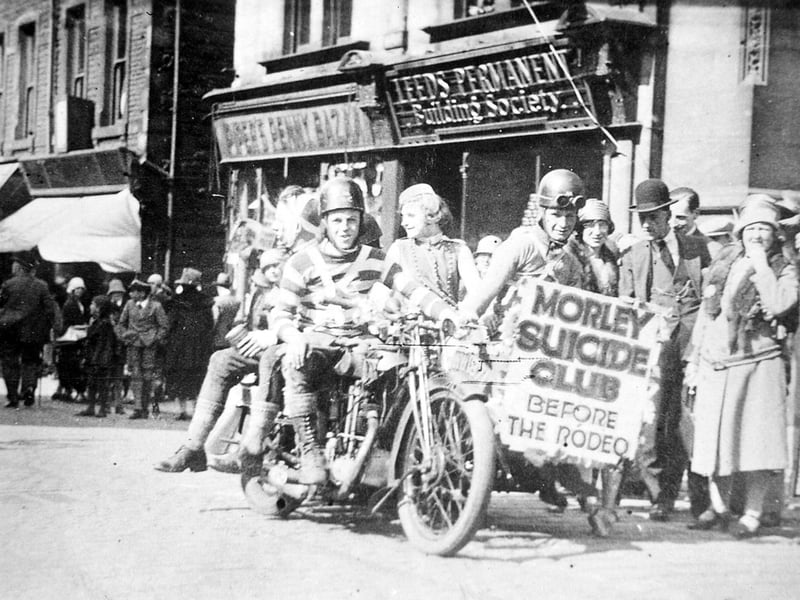 Members of Morley Motor Club parading on motor cycles under the banner "Morley Suicide Club - Before the Rodeo". Morley Motor Club organised motor cylce races in the old Hembrigg Quarry off High Street. As the proceeds were sometimes in aid of Morley Medical Charities they may have been taking part in a Medical Charities Carnival. In the background are nos. 87-89 Queen Street, Pipers Penny Bazaar and the Leeds Permanent Building Society.