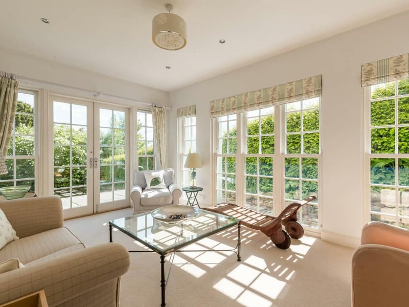 The sun room is lit with banks of windows on two sides, and overlooks the garden.