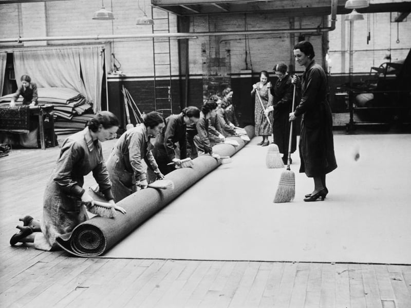 Workers brush both sides of the Coronation carpet as it is rolled at the factory of James Templeton & Co on Glasgow Green. The blue-and-gold carpet, which in total will measure 17-foot wide by 173-foot long, will be transported to London by sea for the coronation of George VI and Queen Elizabeth.