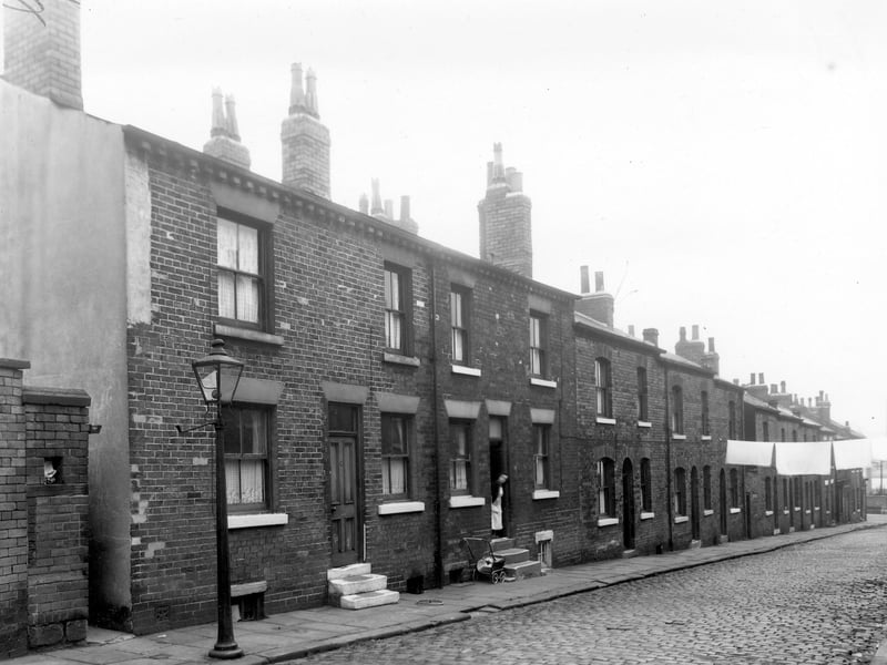 A long view of Lincoln Field Row, numbers start with number 22 on the left and descend right in an evens sequence towards Cherry Row. A narrow passageway cuts through to Lincoln Street and outside toilet facilities are situated alongside. A gas street lamp on the pavement lights the entrance to the passageway at night.