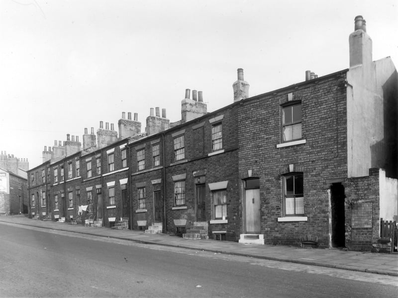 Back-to-back brick constructed terraced housing on Dolly Lane, numbers descend from 24 on the left to 8 on the right. Far left can be seen part of number 28 and the junction with Primrose Place. To the right there is an entrance to a passageway which cuts through to Lincoln Field Terrace. Adjacent to this are brick built outside toilet facilities.