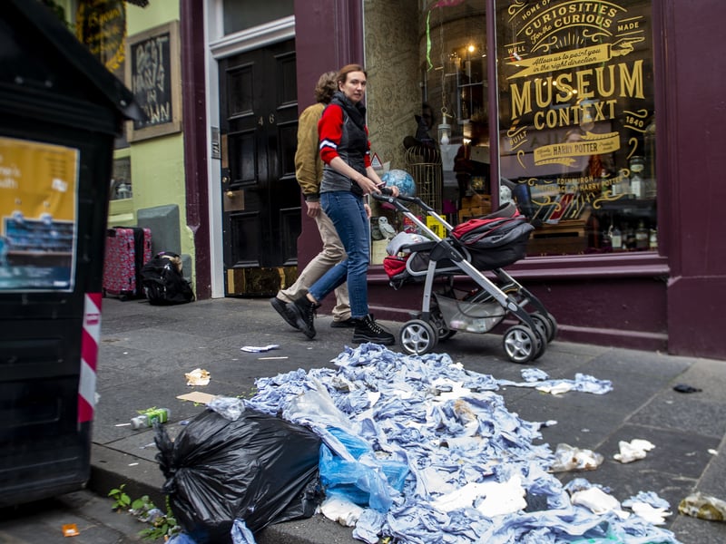 Unions were warning waste would pile up two years ago as workers walked out - and here one passerby on Victoria Street in Edinburgh pushes their buggy past a rubbish bag spilling out old blue paper towel