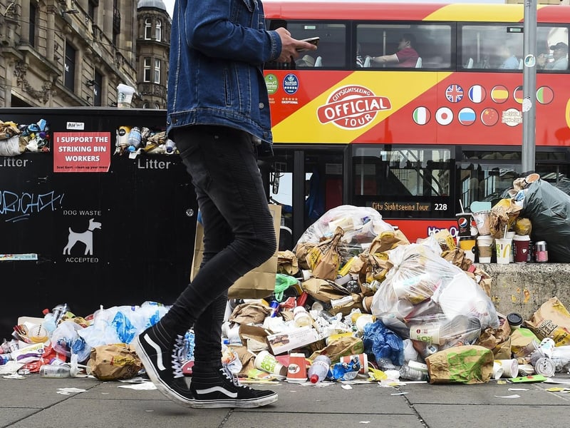 One of Edinburgh's many tourist busses passes the scene on Princes Street, where a pile of rubbish and waste can be seen on the side of the road