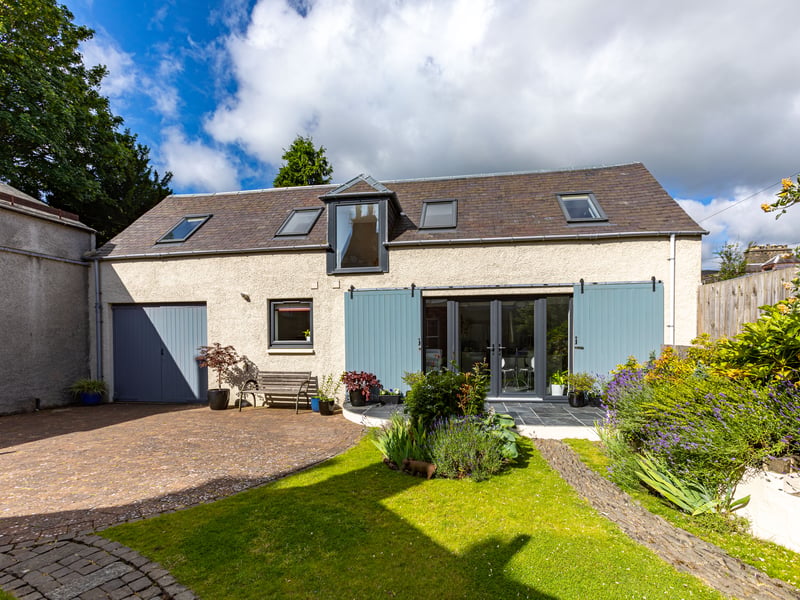 At the back is a two bedrrom coach house conversion with traditional barn shutters hiding modern glass doors, which includes a kitchen and shower room, as well as a double-door garage.