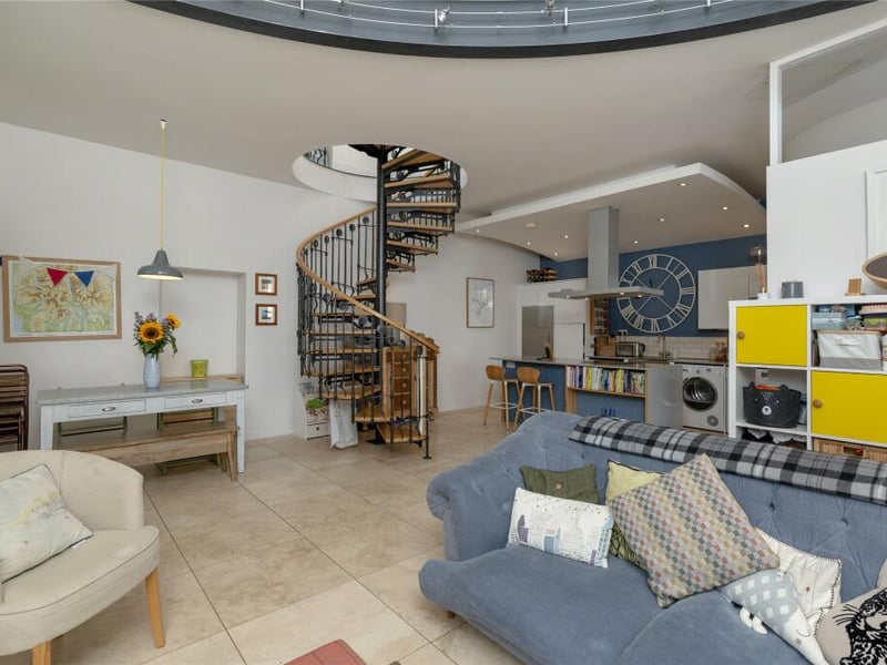 The living space is open plan and also features a kitchen and dining space, with a spiral stair to the mezzanine floor above. 