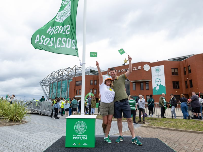 Two Celtic fans wave a flag of their own next to the ceremonial Scottish Premiership flag.