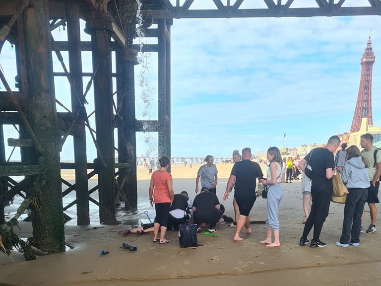 Crowds below Central Pier in Blackpool trying to help teen who fell onto the beach through boards above