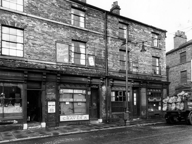 The west side of Hunslet Lane, at the junction with South Row in October 1947. Premises shown are as follows; number 58, D.E. Angus, dining rooms; number 60, D. Johnson, shopkeeper; number 62, N. Johnson, tobacconist and number 64, H. Sidebottom, greengrocer, where a woman looks out of the doorway. To the right a coal lorry is partially visible. It belongs to the business of Lockwood, Hargreaves & Co., coal merchants, of 51 Hunslet Lane.