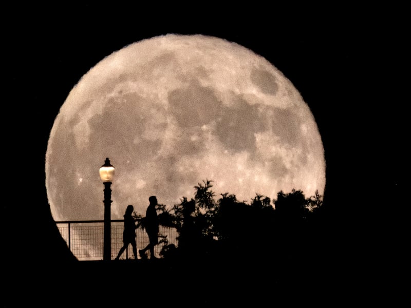 People walk in front of a rising supermoon at Griffith Observatory in Los Angeles