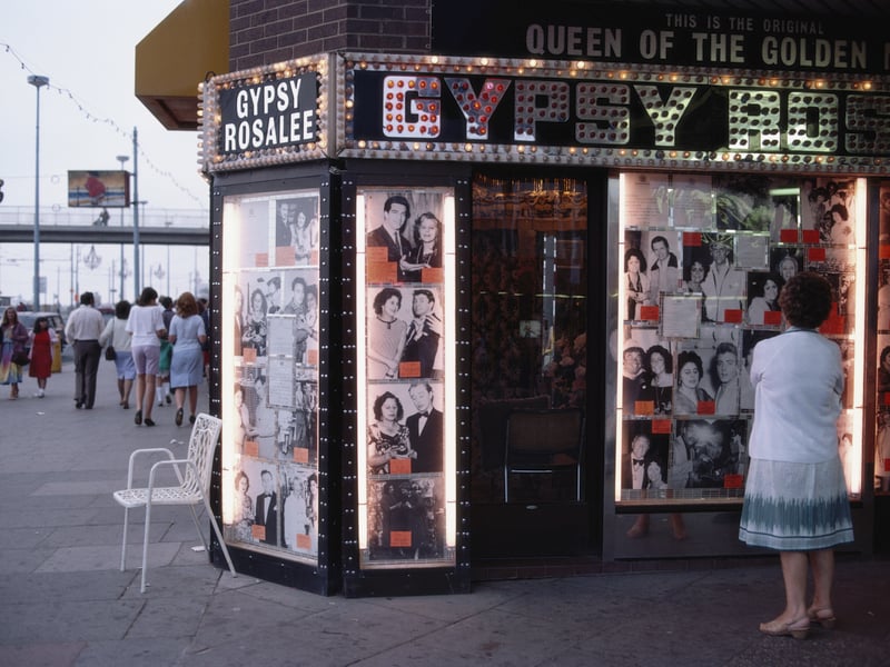 A woman ponders the illuminated front of Gipsy Rosalee's fortune telling service on the golden mile in the seaside resort of Blackpool, Lancashire August 1983. The sign says that Gipsy Rosalee is the queen of the golden mile and the photographs display famous customers including Jimmy Tarbuck and Eddie Large