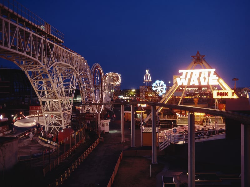 A night view of the illuminated rollercoaster and fun rides including the 'Tidal Wave' at the seaside resort of Blackpool, Lancashire, August 1983