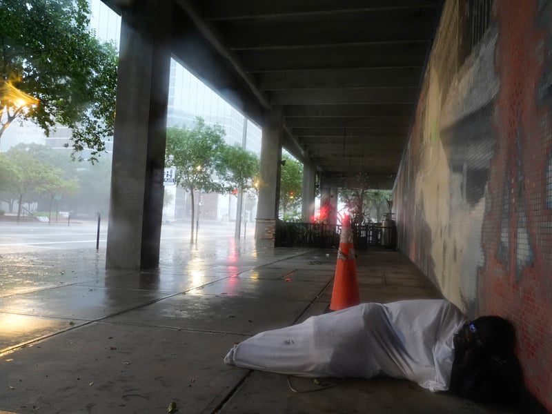 Melvin Lee Hicks, who is homeless, lies under a sheet donated by a nearby hotel, as he shelters alongside a parking garage in downtown Tampa, Florida, during the approach of Hurricane Milton.