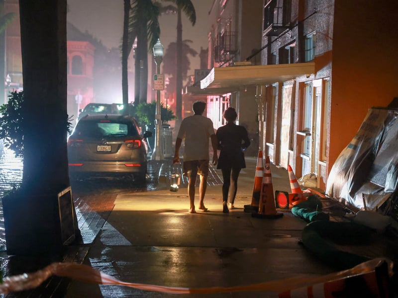 People walk along a street through the wind and rain after powercuts due to Hurricane Milton making landfall in the Sarasota area of Florida.