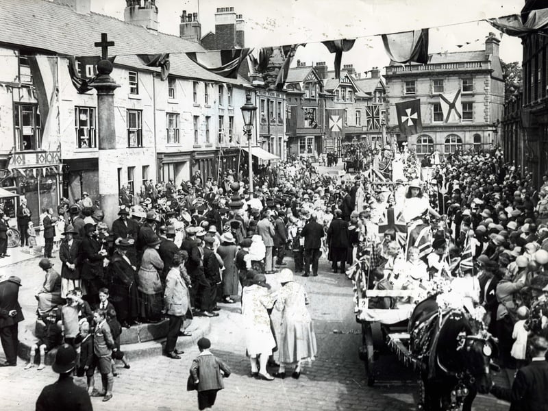 Poulton Gala procession through the Market Place in 1929.
The Manchester and County Bank at the far end of the square replaced houses, but was later demolished creating a view of St Chad's Church. The stepped cross is providing a vantage point for onlookers.
The colourful procession includes a young Britannia and, in the background on one of the floats, is a recreation of the market cross. Like many of the buildings in the Square, the Williams Deacons Bank building still stands but is now the home of the Royal Bank of Scotland